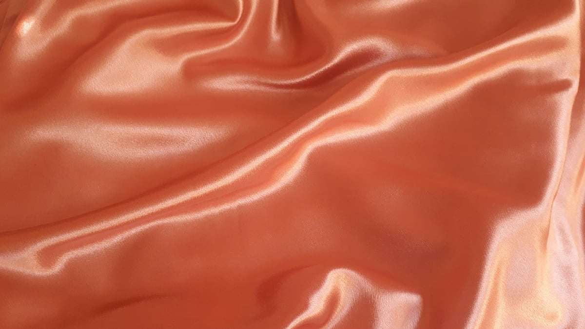 Peach satin folds catch the light, with bright highlights and soft shadows.