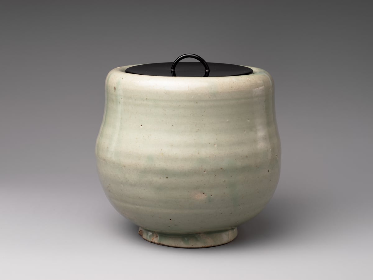 A pale green ceramic water jar with a black lid and curved handle.