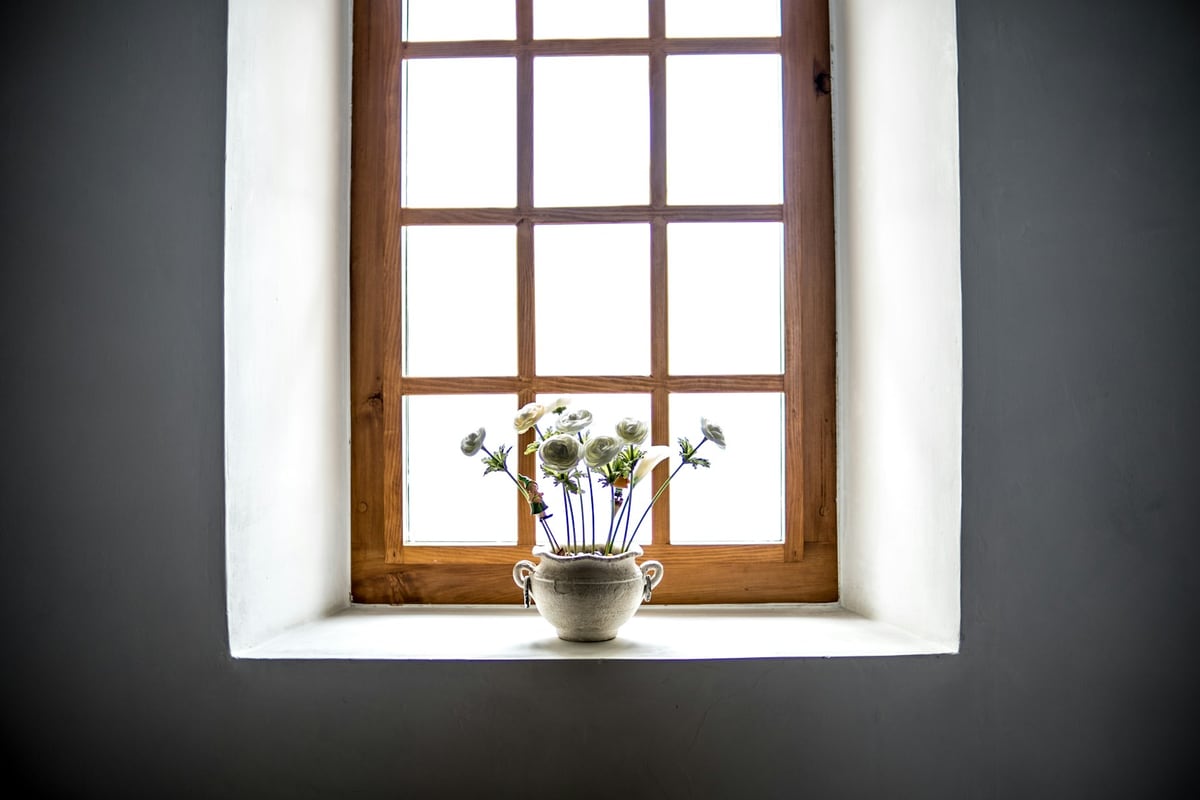 White flowers in a ceramic vase beneath a wooden window.